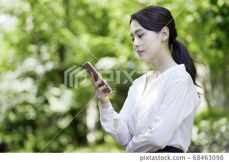 看智能手機的少婦反對新鮮的綠樹 看智能手機的少婦反對新鮮的綠樹 68463098