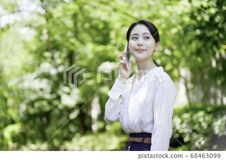 看智能手機的少婦反對新鮮的綠樹 看智能手機的少婦反對新鮮的綠樹 68463099