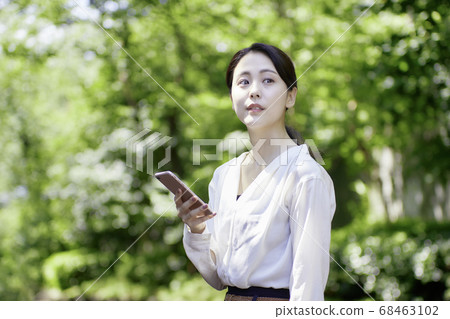看智能手機的少婦反對新鮮的綠樹 看智能手機的少婦反對新鮮的綠樹 68463102