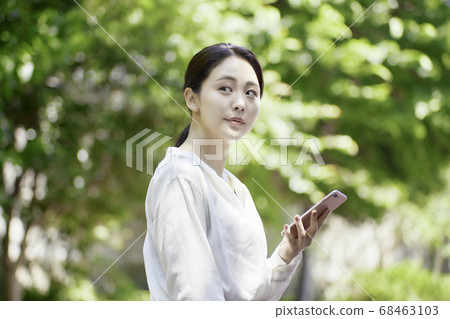 看智能手機的少婦反對新鮮的綠樹 68463103