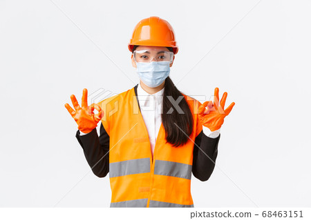 Covid-19 safety protocol at enterpise, construction and preventing virus concept. Satisfied asian female engineer, industrial woman face mask showing okay gesture, well done, praising good work 68463151