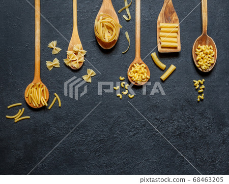 Various types of dry pasta on spoons on a black background with a place for the signature 68463205