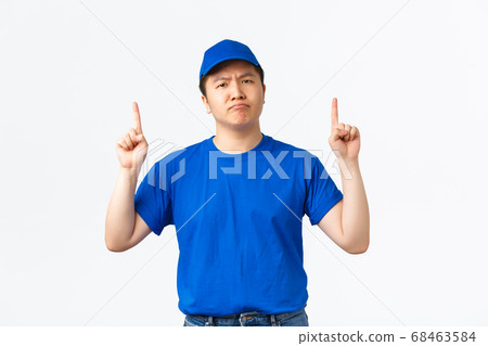 Skeptical and doubtful courier in blue cap and t-shirt having doubts, sulking and frowning with disbelief as pointing fingers up. Delivery guy being suspicious about promotion, white background Skeptical and doubtful courier in blue cap and t-shirt having doubts, sulking and frowning with disbelief as pointing fingers up. Delivery guy being suspicious about promotion, white background 68463584