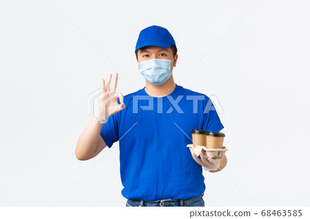 Contactless delivery, covid-19 shipping, preventing virus concept. Friendly asian male courier in uniform, medical mask and gloves, handing coffee takeaway and show okay gesture, guarantee safety Contactless delivery, covid-19 shipping, preventing virus concept. Friendly asian male courier in uniform, medical mask and gloves, handing coffee takeaway and show okay gesture, guarantee safety 68463585