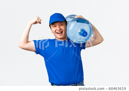 Office and home delivery and employees concept. Upbeat smiling asian courier in blue uniform, flex biceps, postman tell he is strong, carry heavy bottle with clean water on shoulder, white background 68463619