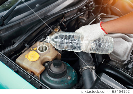 Mechanic hands fill fresh water into windscreen in car engine room. 68464192