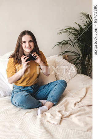 Young beautiful girl student in an orange T-shirt and blue jeans sits on bed with pillows and listens to an audiobook, music, podcast on headphones. Self-education concept at home during quarantine. Young beautiful girl student in an orange T-shirt and blue jeans sits on bed with pillows and listens to an audiobook, music, podcast on headphones. Self-education concept at home during quarantine. 68473890