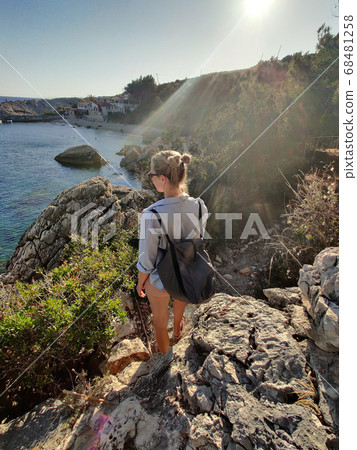 Young active feamle tourist wearing small backpack walking on coastal path among pine trees enjoing beautiful costal view of Velo Zarace beach on Hvar island, Croatia. Travel and adventure concept Young active feamle tourist wearing small backpack walking on coastal path among pine trees enjoing beautiful costal view of Velo Zarace beach on Hvar island, Croatia. Travel and adventure concept 68481258