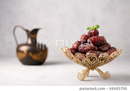 Date Fruits or Kurma in vintage arabic dish and jug of water at grey concrete background Date Fruits or Kurma in vintage arabic dish and jug of water at grey concrete background 68483700