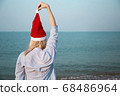 Girl in a red Christmas hat on the beach next to the sea. Holiday concept. 68486964