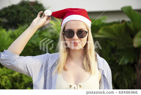 Girl in a red Christmas hat next to the swimming pool with blue water. Holiday concept. 68486966
