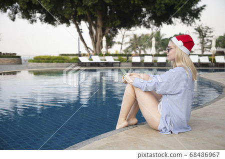 Girl in a red Christmas hat next to the swimming pool with blue water. Holiday concept. 68486967