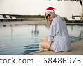 Girl in a red Christmas hat next to the swimming pool with blue water. Holiday concept. 68486973
