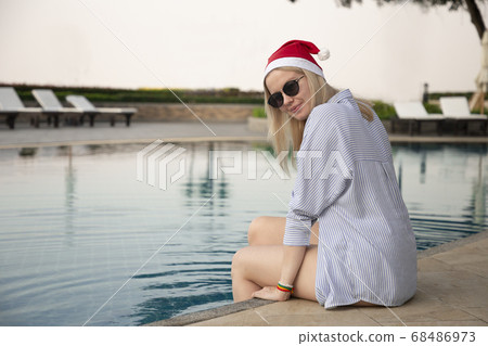 Girl in a red Christmas hat next to the swimming pool with blue water. Holiday concept. 68486973