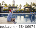 Girl in a red Christmas hat next to the swimming pool with blue water. Holiday concept. 68486974