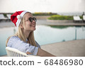 Girl in a red Christmas hat next to the swimming pool with blue water. Holiday concept. 68486980