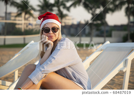 Girl in a red Christmas hat on the beach next to the sea. Holiday concept. Girl in a red Christmas hat on the beach next to the sea. Holiday concept. 68487019