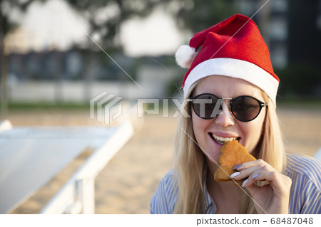 Girl in a red Christmas hat on the beach next to the sea. Holiday concept. Girl in a red Christmas hat on the beach next to the sea. Holiday concept. 68487048