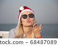 Girl in a red Christmas hat on the beach next to the sea. Holiday concept. 68487089