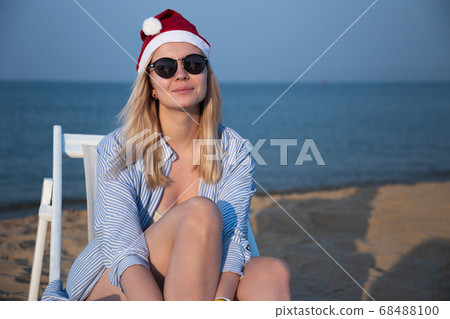 Girl in a red Christmas hat on the beach next to the sea. Holiday concept. Girl in a red Christmas hat on the beach next to the sea. Holiday concept. 68488100