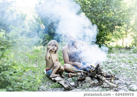 Father and little cute son sitting by the fire in the forest. Father and little cute son sitting by the fire in the forest. 68489959