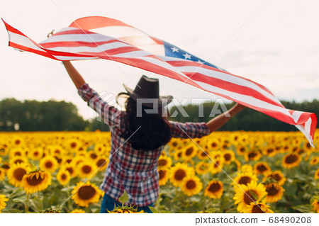 Young woman with American flag in the sunflower field. 4th of July Independence Day USA concept. Young woman with American flag in the sunflower field. 4th of July Independence Day USA concept. 68490208