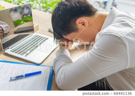 Exhausted businessman sitting with laptop and documents at office table Exhausted businessman sitting with laptop and documents at office table 68491136