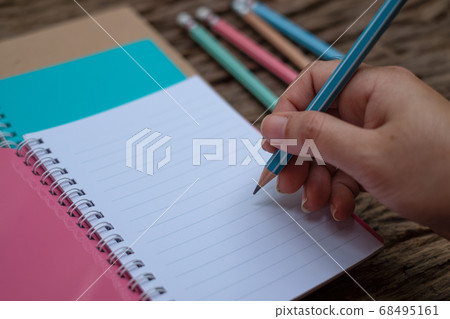 Hand holding pencil and book at wood desk background Hand holding pencil and book at wood desk background 68495161