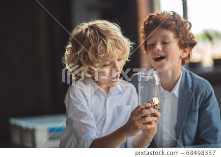 Two boys looking at the jar with coins and looking interested Two boys looking at the jar with coins and looking interested 68498337