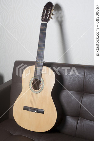 Acoustic classic guitar leaning on brown leather Acoustic classic guitar leaning on brown leather 68500667