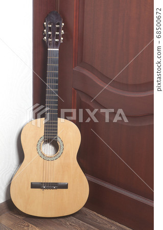 Acoustic guitar leaning against a wooden door 68500672