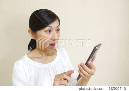Middle-aged woman with a surprised expression operating a smartphone 68500740