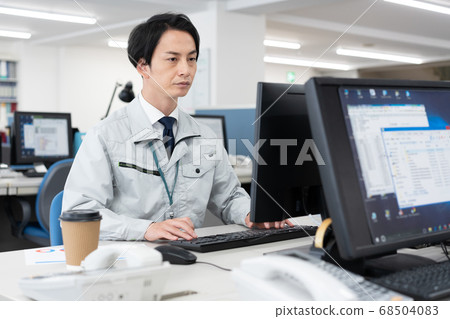 Young men in work clothes operating a personal computer work in the company Young men in work clothes operating a personal computer work in the company 68504083