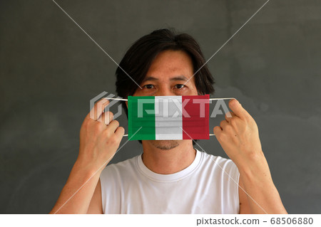 A man with Italy flag on hygienic mask in his hand and lifted up the front face on yellow background A man with Italy flag on hygienic mask in his hand and lifted up the front face on yellow background 68506880