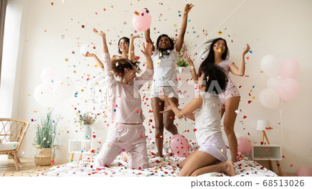 Multiethnic women wearing pyjamas dancing on bed under falling confetti Multiethnic women wearing pyjamas dancing on bed under falling confetti 68513026