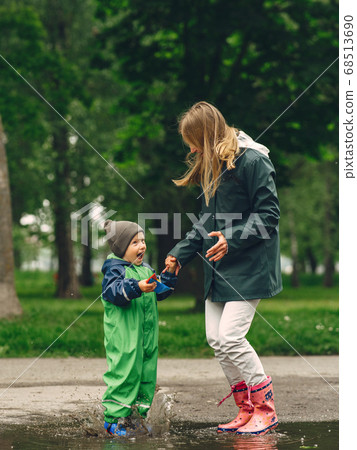 Funny kid in rain boots playing in a rain park 68513690