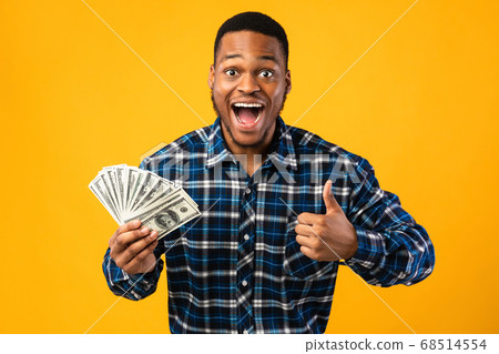 Excited African Guy Holding Money Gesturing Thumbs-Up Over Yellow Background 68514554