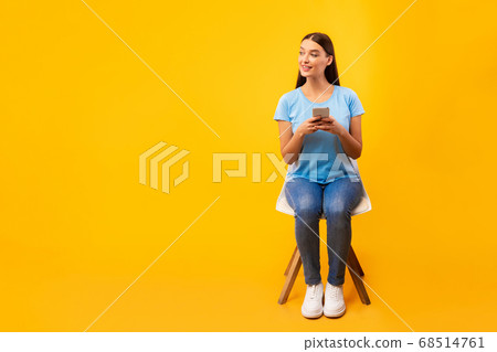 Studio shot of girl sitting on chair with phone 68514761