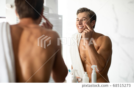 Handsome guy looking in the mirror applying cream Handsome guy looking in the mirror applying cream 68515273