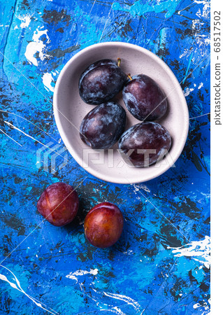 Fresh sweet plum fruits in white bowl on blue abstract background 68517502