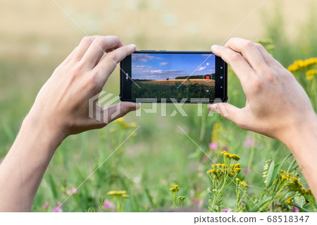 Holding smart phone with two hands shooting nature Holding smart phone with two hands shooting nature 68518347