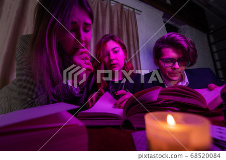 Two women and a guy are reading a mysterious books, close view Two women and a guy are reading a mysterious books, close view 68520084