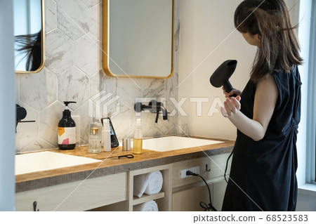 A woman drying her hair with a dryer. A woman drying her hair with a dryer. 68523583