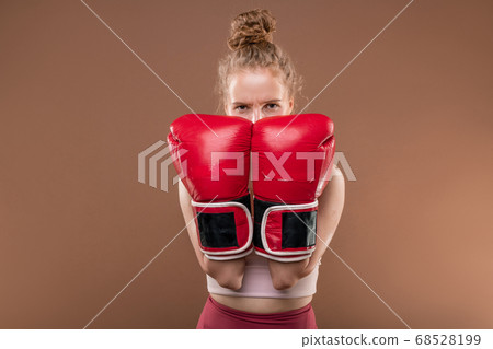 Young blond sportswoman in tracksuit keeping hands in boxing gloves by her face 68528199