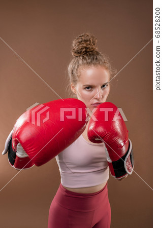 Young serious active woman in tracksuit and boxing gloves doing kicks and hits 68528200
