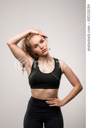 Fit young woman in black tracksuit touching her long blond curly hair 68528284
