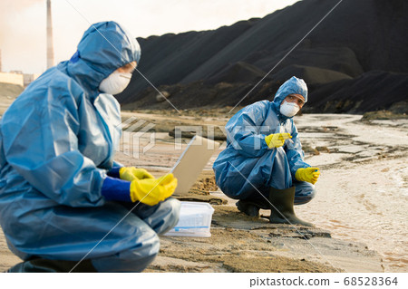Young female ecologist holding sample of dirty water while looking at colleague 68528364