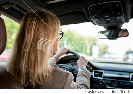 Woman with blond hair looking through front window while driving for meeting 68528508