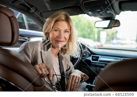 Happy mature female sitting by steer in car and looking at someone on backseat Happy mature female sitting by steer in car and looking at someone on backseat 68528509