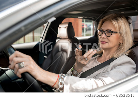 Blond mature female holding smartphone by her mouth and recording voice message 68528515